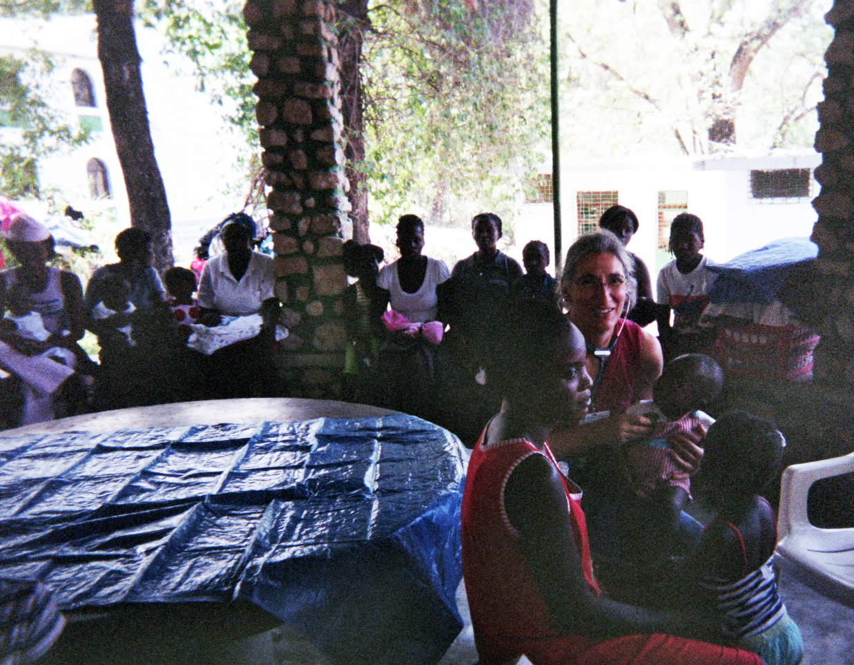 <em><strong>Dr. Hélène Rousseau attending to an infant at the camps. Behind them, women and children wait their turn. (Photo courtesy Dr. Hélène Rousseau)</em></strong>